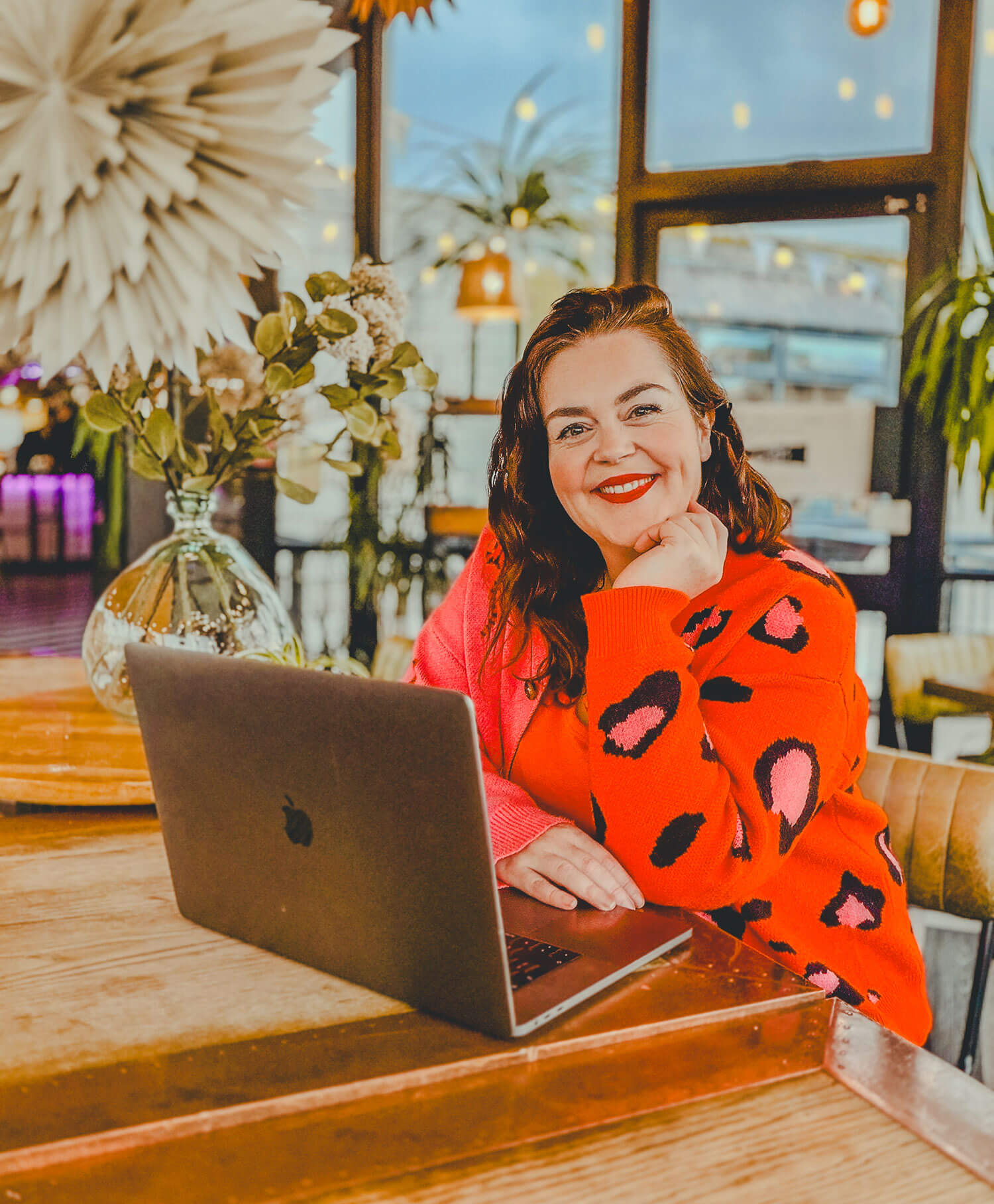 Photographer Rosie Parsons sits while blogging at her laptop in a bright leopard print orange and pink patterned jumper