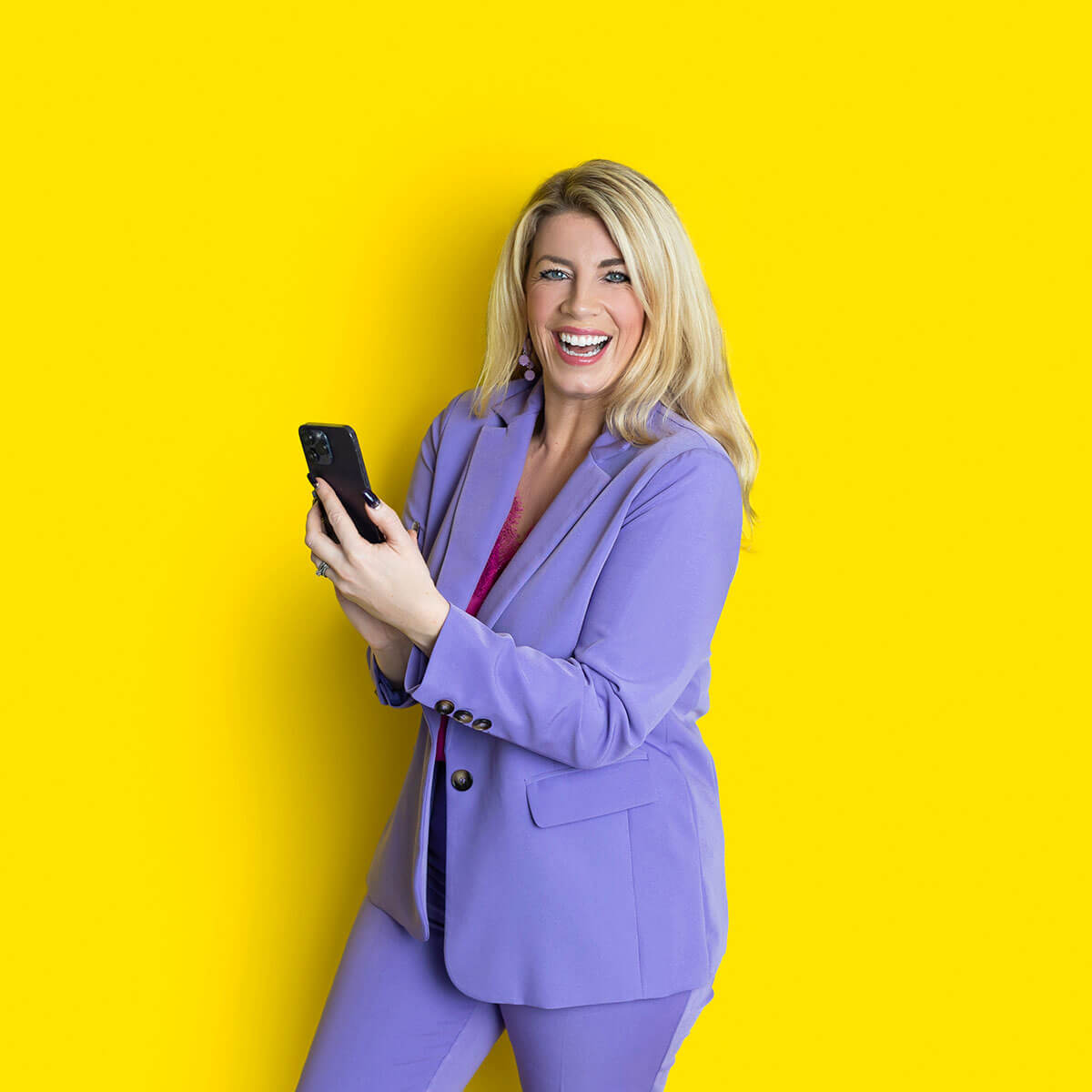 Personal branding photo of a woman wearing a lilac suit while laughing and looking at her phone in a colourful studio setting