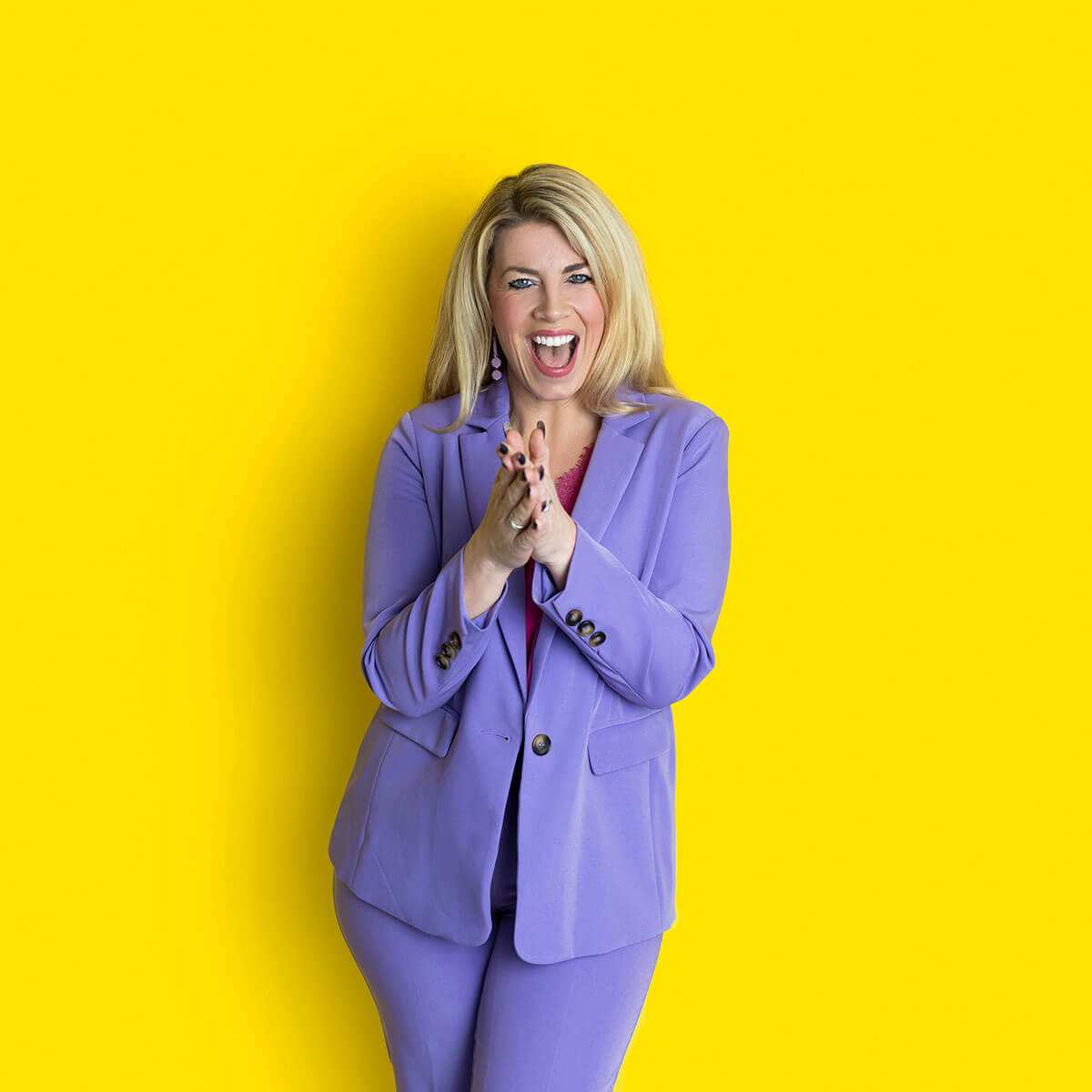 Studio portrait of Laura Brunton, coach and business mentor, wearing a lilac suit while clapping her hands and smiling in a colourful branding session