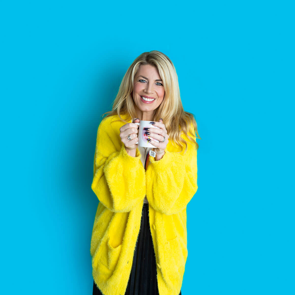Studio branding portrait of Laura Brunton, coach and business mentor, wearing a bright yellow coat and holding a cup