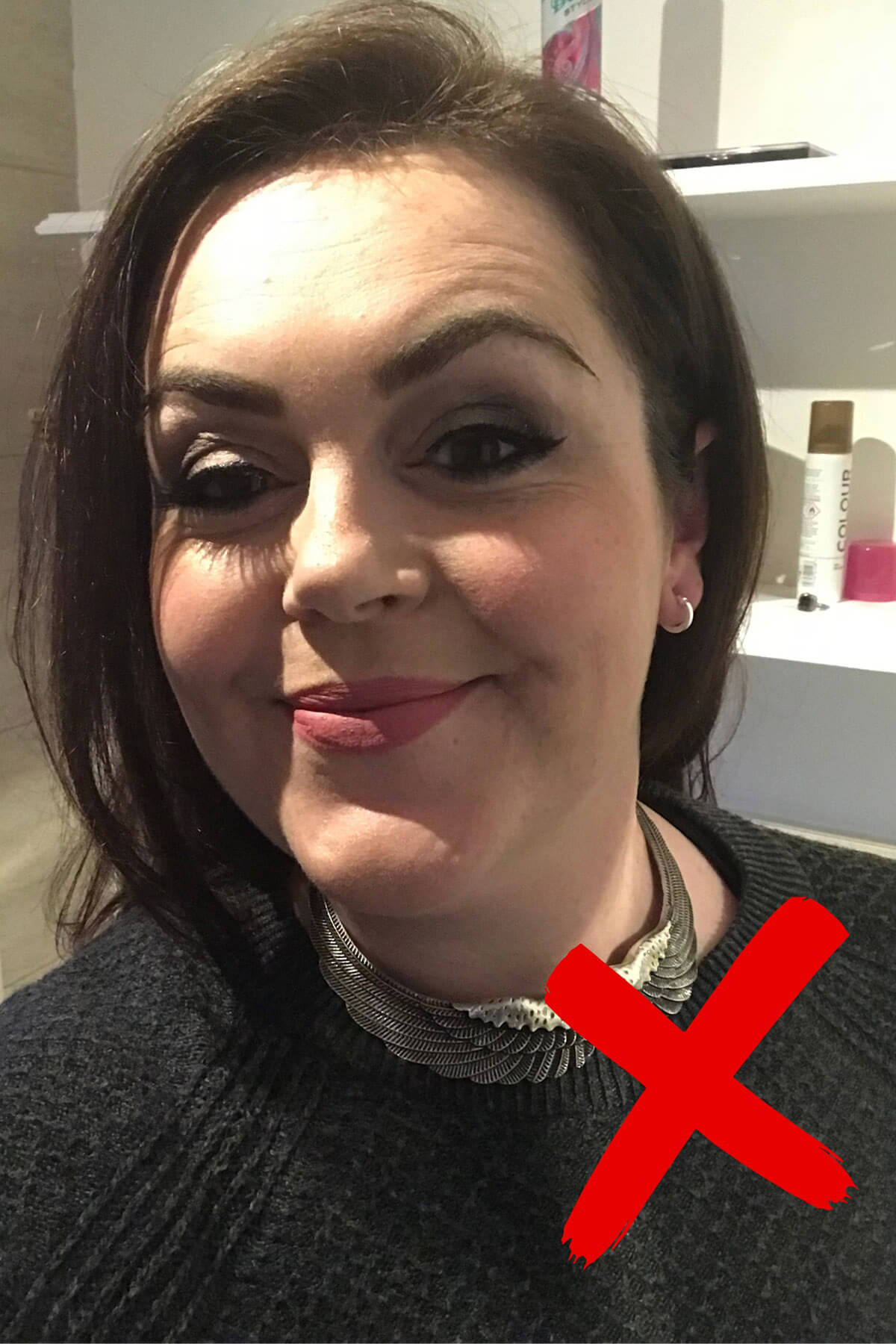 Example of unflattering selfie lighting marked with red X, showing harsh overhead bathroom light creating shadows on face, with cluttered background of toiletries visible – demonstrating common selfie mistakes to avoid