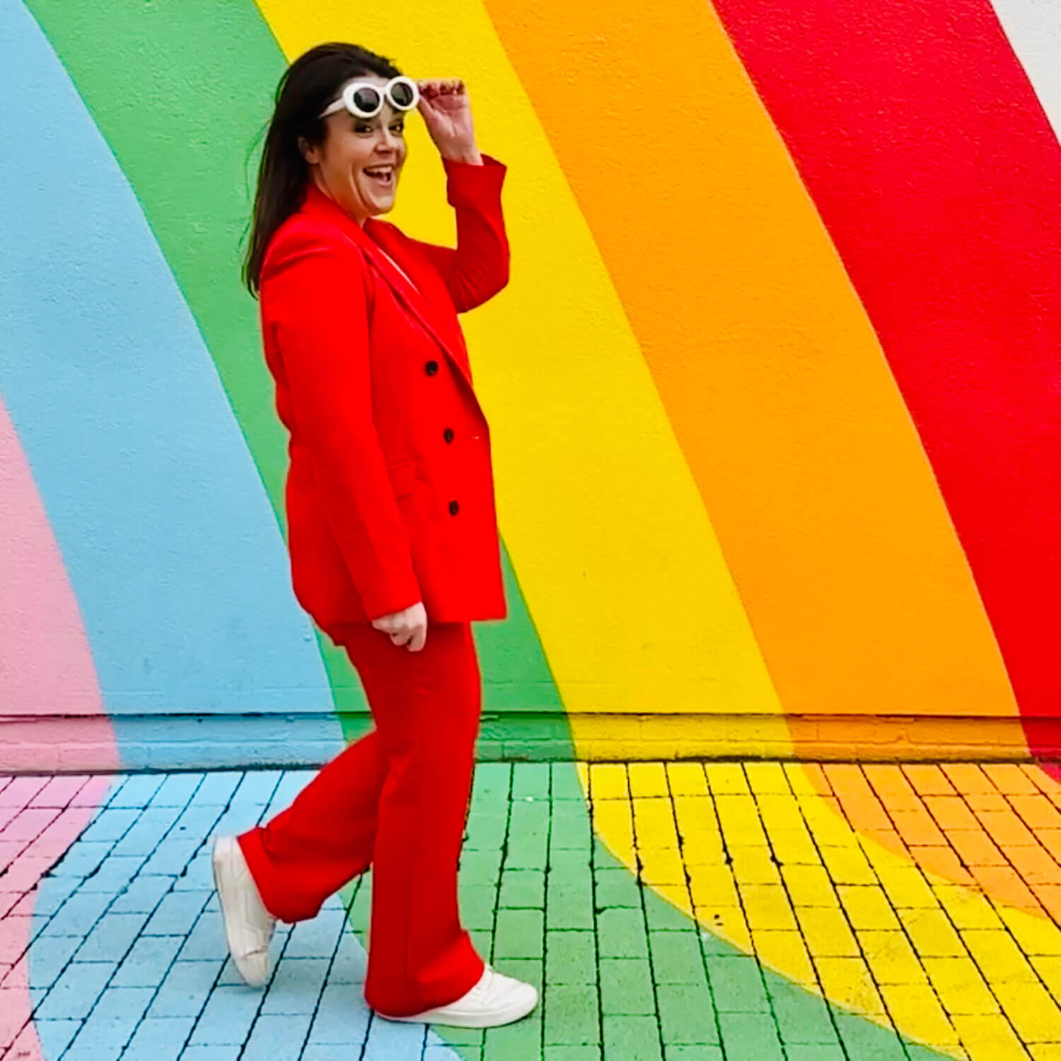 Small business blogger Rosie Parsons in a bold red suit and white sunglasses, laughing in front of a rainbow-striped wall - inspiration for how to start a blog for beginners